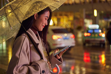 夜晚走路下雨天站在路边使用手机的女性背景