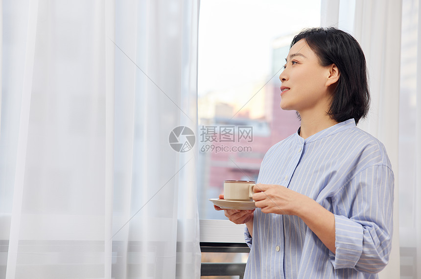 短发中年女性窗前喝咖啡图片