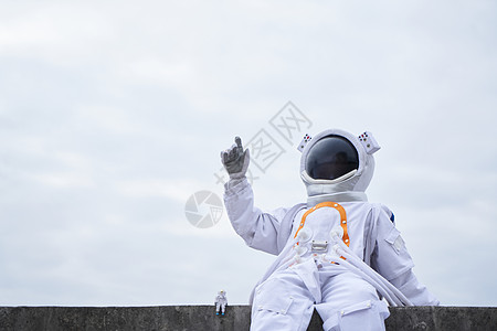穿着宇航服的男性坐在海边手指远方图片