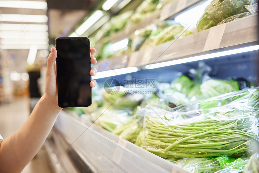 蔬菜摊前展示手机屏幕特写图片