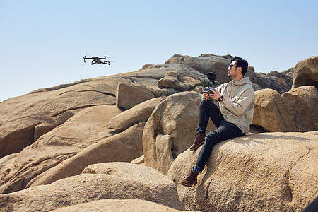 航拍摄影师坐在山顶使用无人机拍摄背景图片
