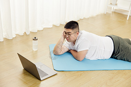 胖子男生瑜伽垫上看电脑视频教程图片