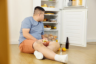 肥胖男士冰箱旁吃汉堡吃撑图片