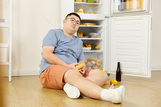 贪吃的肥胖男青年坐在冰箱旁图片