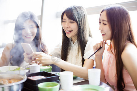 年轻妇女组吃火锅和拍照通过电话图片
