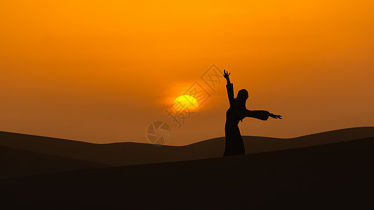 鸣沙山日落夕阳下沙漠山顶跳舞的女人剪影背景