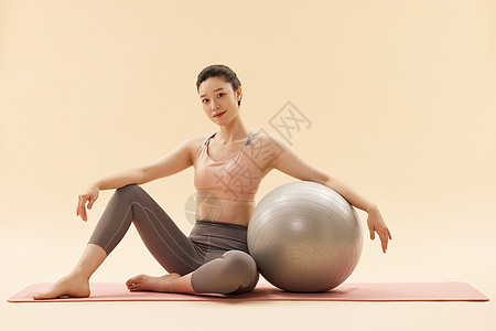 倚靠在瑜伽球边上的健身女性图片