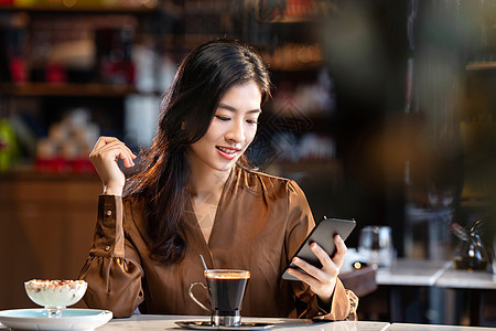 咖啡馆内边喝咖啡边使用手机的青年女人图片