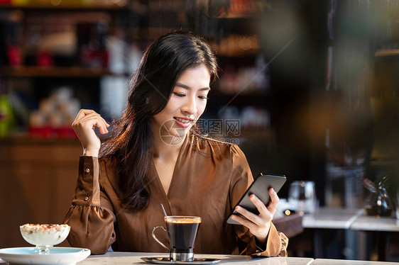 咖啡馆内边喝咖啡边使用手机的青年女人图片