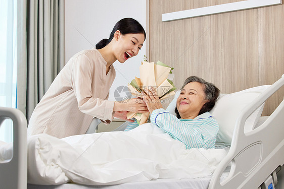 手拿花束的青年女性探望生病住院的老人图片