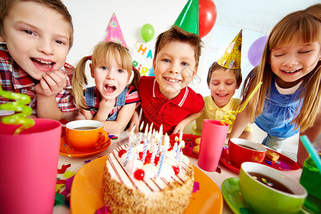 一群可爱的孩子聚集在生日蛋糕周围带着图片