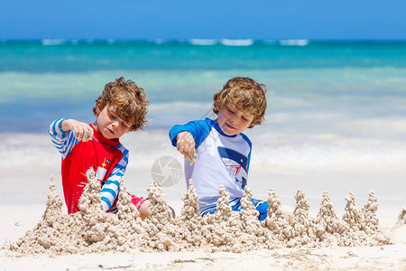 两个小男孩在牙买加热带海滩上兴高采烈地建了一座沙滩城堡图片