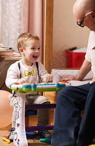 一个漂亮的笑着的小孩坐在卧室的一张小桌子旁和祖父玩耍的背景图片