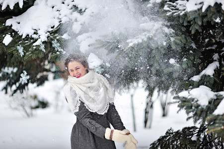 美丽的女人在冬天针织连指手套扔雪图片