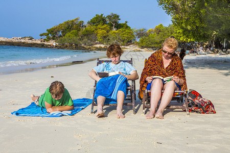 在美丽的海滩上享受阳光放松和阅读书本的家庭正图片