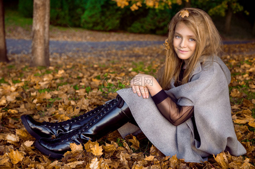 穿着大衣和靴子的可爱小女孩坐在秋天背景图片