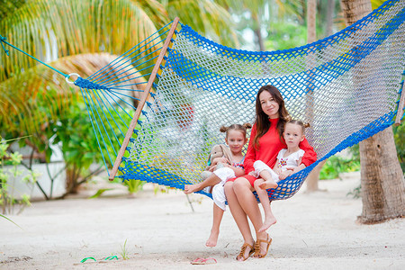 年轻美丽的母亲和可爱的小女儿们在热带海滩图片