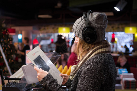 在黑乙烯店的帽子和大衣上听耳机音乐的年轻背景图片