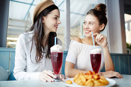 快乐的年轻妇女坐在咖啡厅喝鸡尾酒图片