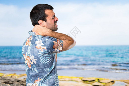 英俊的男人在海滩上有脖子痛的花衬衫背景图片