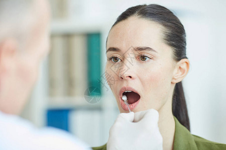 从年轻女口腔和喉咙抽取样本的男医生在诊所进行检测时图片
