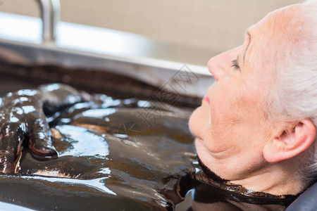 享受泥浴替代疗法的老妇人背景图片