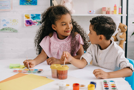 非裔美国小孩在课堂上用涂料和油漆刷子看对方的绘画照片图片