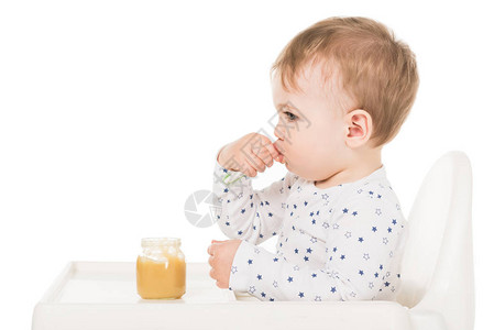 男婴从罐子里吃果泥坐在白色背景的高脚图片