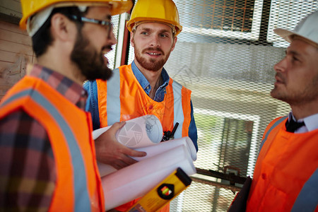 三名戴防护头盔和背心的工人站在建筑工地的电梯井中讨论开发进度手图片