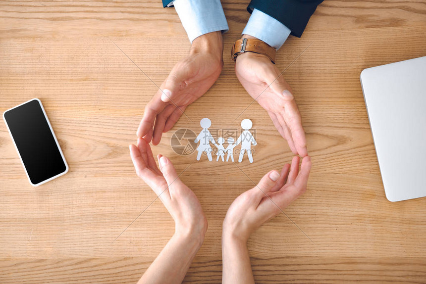 保险代理人和女手的部分观点与木桌面上的家庭纸模型图片