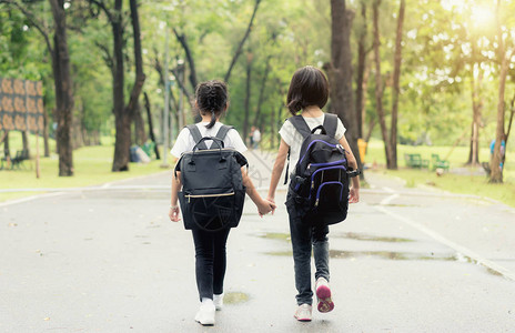 两个小学生齐头并进两个背着书包的女孩秋天温暖的一天回到学校一图片