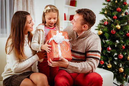 美丽的年轻微笑父母在家里给他们可爱的快乐小女儿送礼物过圣诞节或庆祝图片