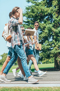 青少年学生与书籍和小工具一起在公园里走图片