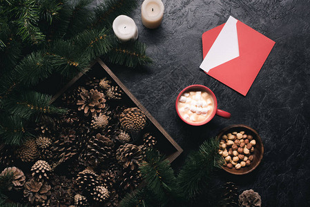 新年卡片木箱蜡烛坚果信封和黑桌顶上加棉花糖的可咖啡杯中背景