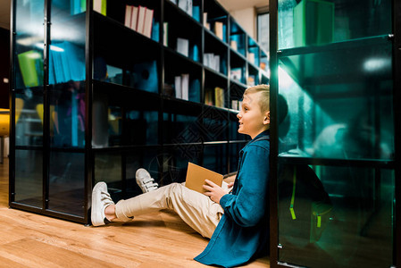 坐在地板上微笑的男孩和图书馆阅读图片