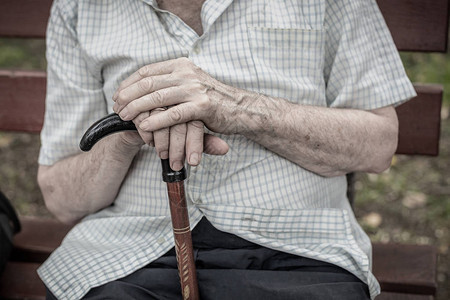 老人坐在户外的长木凳上老人手里拿着拐杖贫穷孤独背景图片