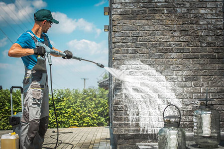 用特殊的清洁洗涤剂洗刷砖屋壁压力30多岁的白人男子负责楼梯的维修工作背景图片