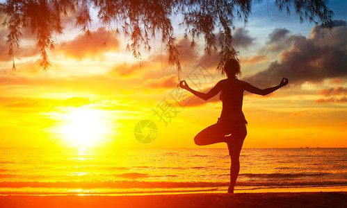 日落时在沙滩上练习瑜伽的年轻女子图片