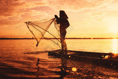 亚洲渔民在木船上使用网钓在河中撒网日落或日出图片