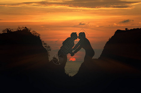 情侣牵手在美丽的夕阳背景下亲吻的剪影图片
