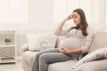 在沙发上坐着头痛的年轻孕妇妊娠症状预期父母概念复图片