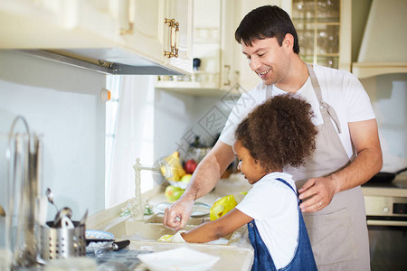 小女孩在厨房旁边与父亲一起洗盘图片