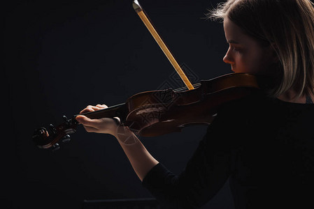 集中的年轻女子在黑暗中用大提琴和玩大提琴图片