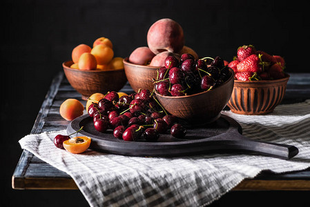 用樱桃草莓桃子和杏子放在黑色木桌上的碗选择焦点图片