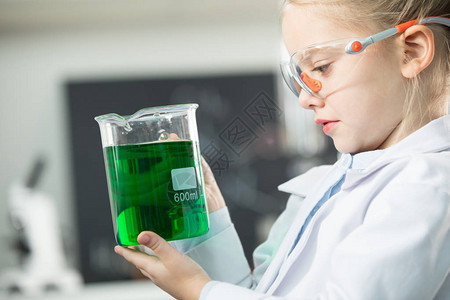 身着实验室大衣和保护眼镜拿着绿色试剂的玻图片