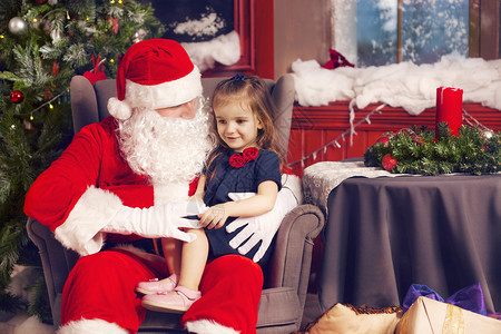 小女孩在圣诞树附近的圣诞老人中讲述图片