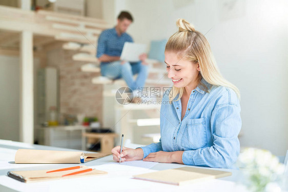 快乐的年轻设计师在工作室坐在桌边画纸时图片