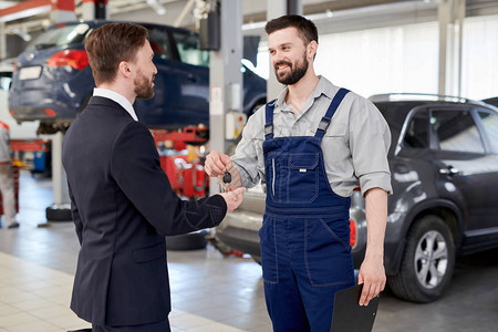 向站在现代汽车服务和修理中心的商人提供车钥匙的笑式胡须机械图片