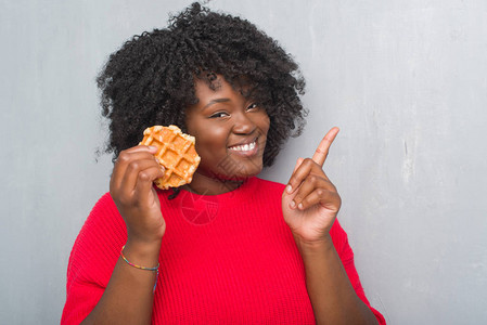 青非洲美裔年轻女在灰色的黑面墙上食着饼图片