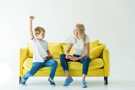 在白色黄沙发上赢得视频游戏后快乐的儿子图片